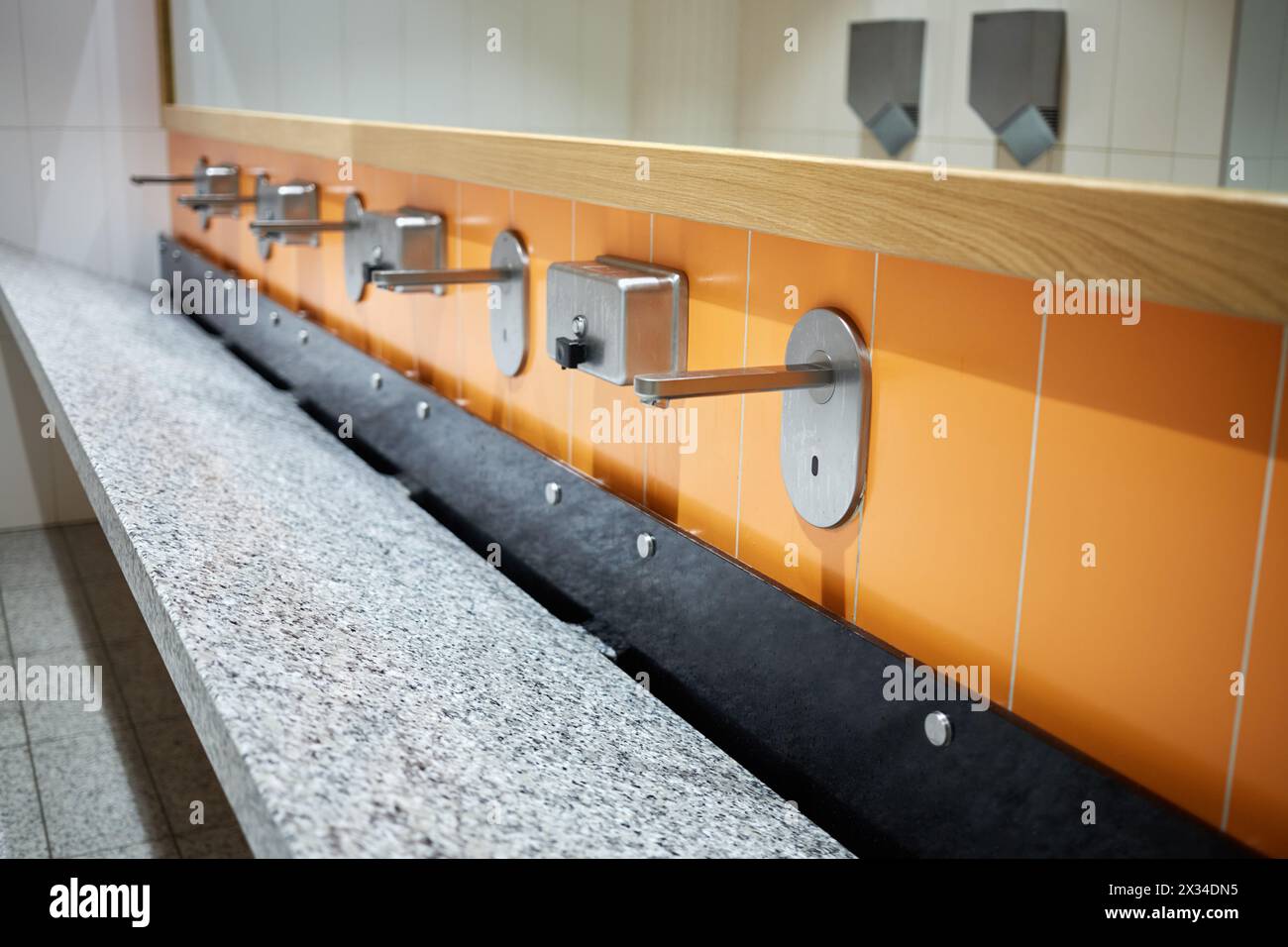 Großes Waschbecken mit mehreren Wasserhähnen und Spiegel darüber. Stockfoto