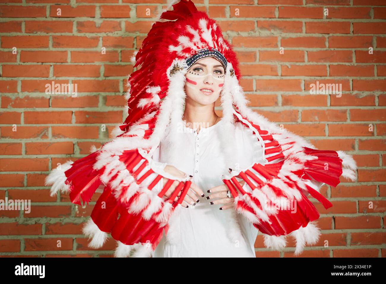 Eine junge Frau mit einem Hut aus Federn und Armen, die mit Federn wie Flügeln bedeckt sind. Stockfoto
