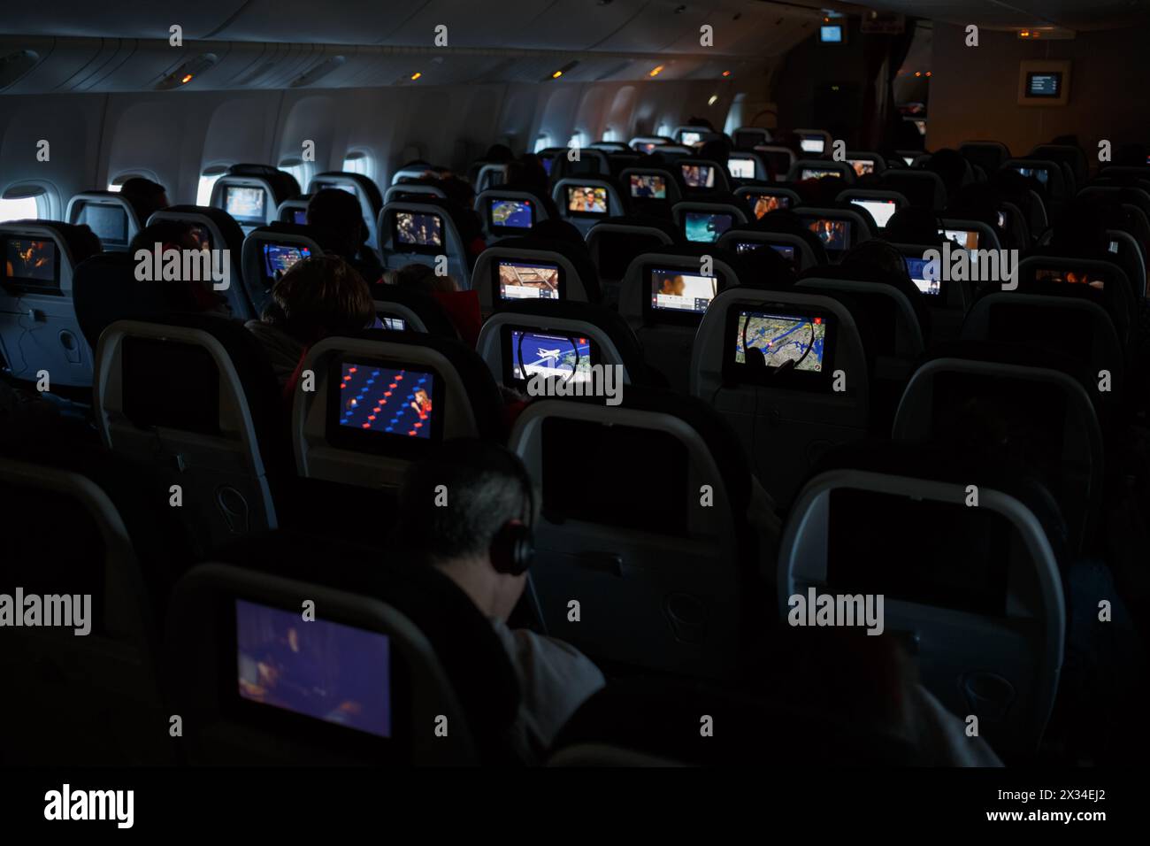 Passagiere sehen Filme in einer dunklen Flugzeugkabine Stockfoto