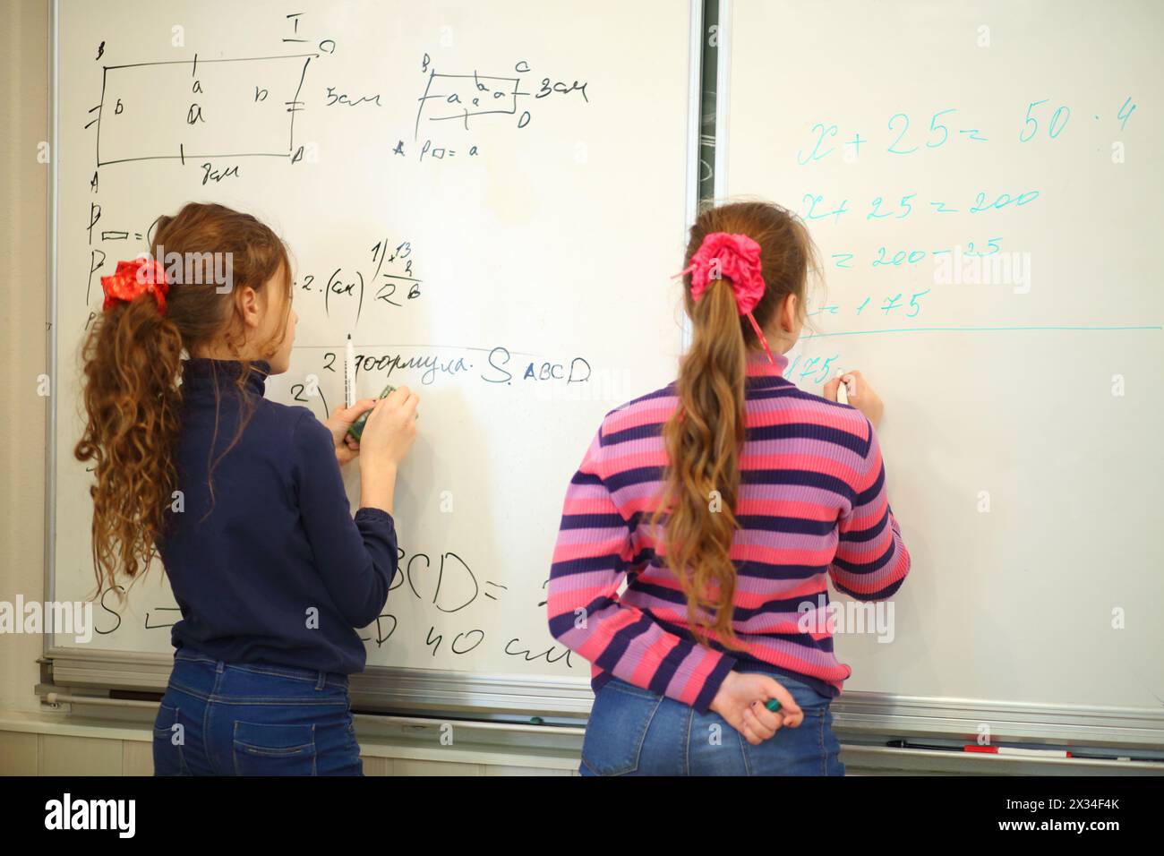 Schulmädchen schreiben auf Tafel mit geometrischen Beispielen und Übungen im Klassenzimmer, Rückansicht, Text - Formel, Fokus auf Text Stockfoto