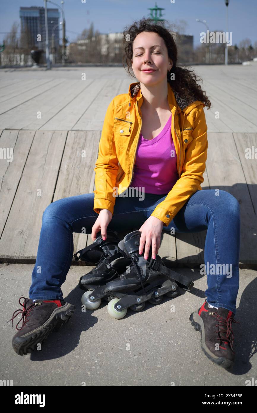 Glückliche hübsche Frau sitzt mit Rollschuhen und Freuden an sonnigen Tagen im Freien Stockfoto