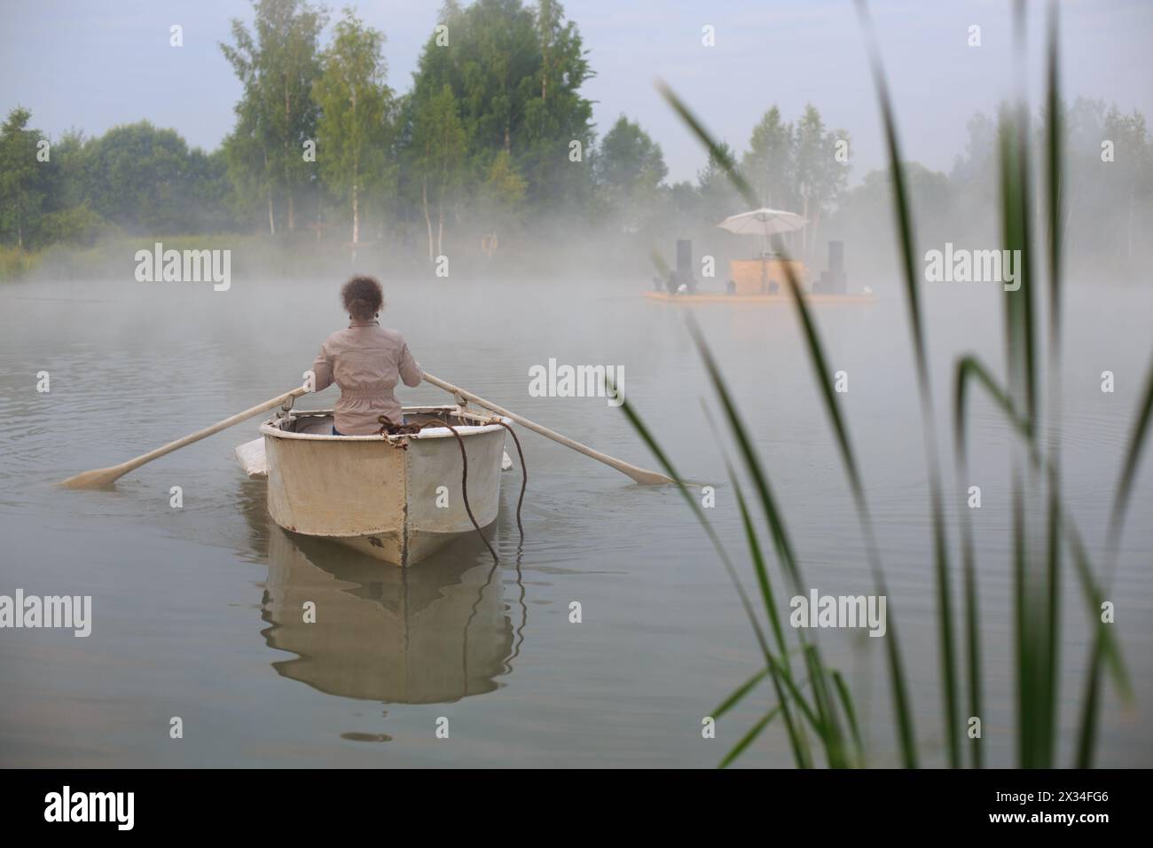 Junge Frau im Boot am Frühsommermorgen, die den Fluss hinunter zur Küste schwimmt Stockfoto