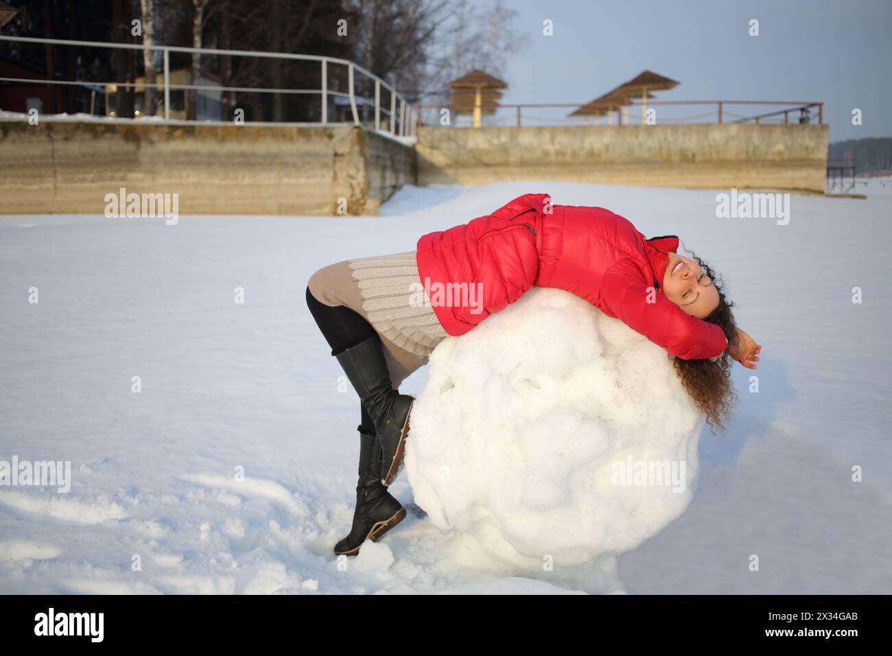 Eine Frau in einer roten Jacke, die auf dem Rücken auf einem großen Schneeball liegt Stockfoto