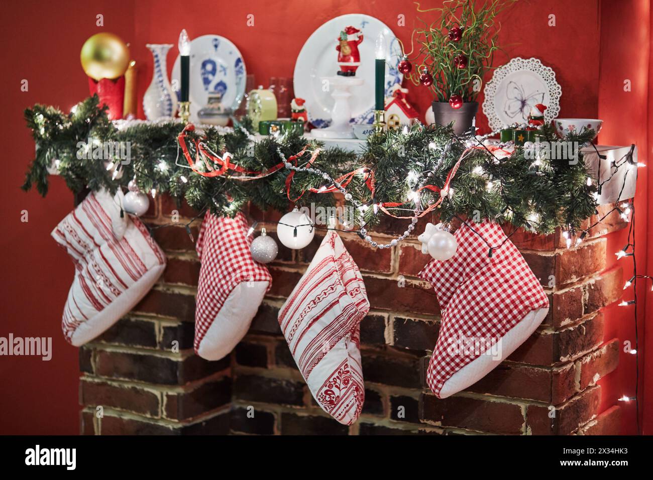 Kamin mit Schrankwand, dekoriert zu weihnachten mit Nadelbäumen, Kugeln, Kerzen, Tellern, Geschenkstiefeln. Stockfoto