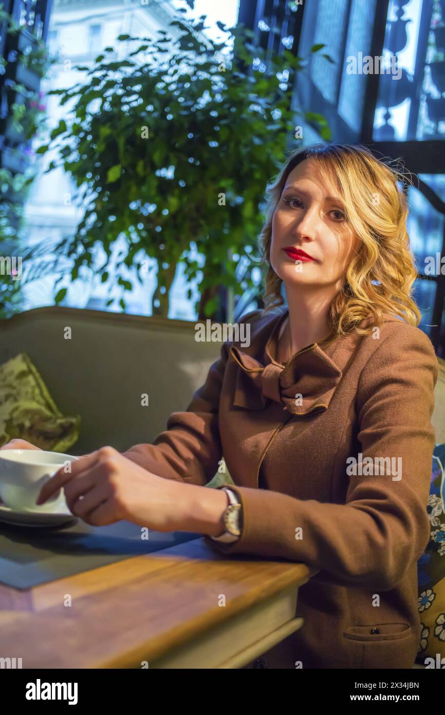 Eine mittelgroße blonde Frau sitzt mit Tee und schaut im Restaurant in die Kamera Stockfoto