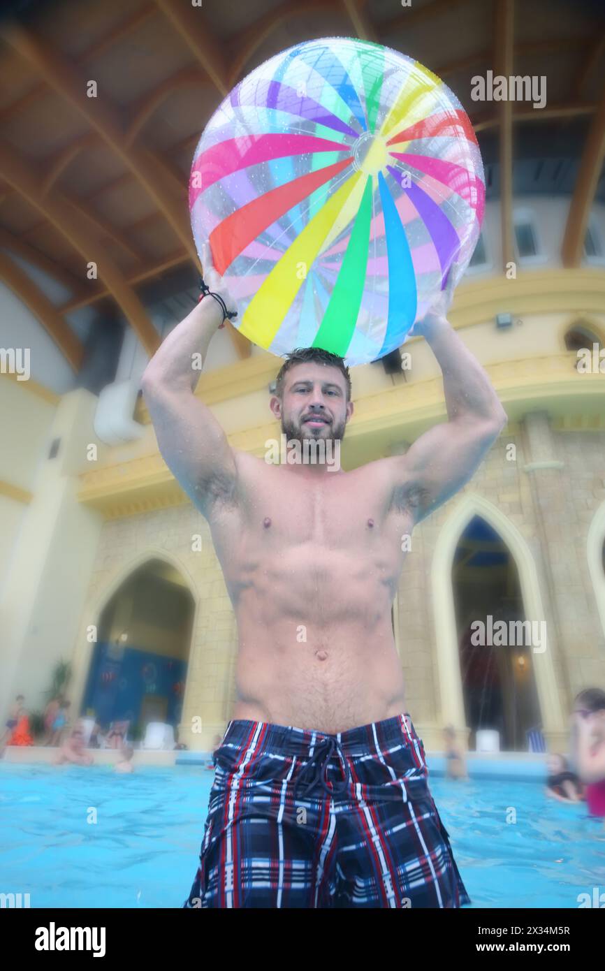 Der Mann hielt einen großen Ballon im Pool mit Badegästen am Aquapark, Blick von unten Stockfoto