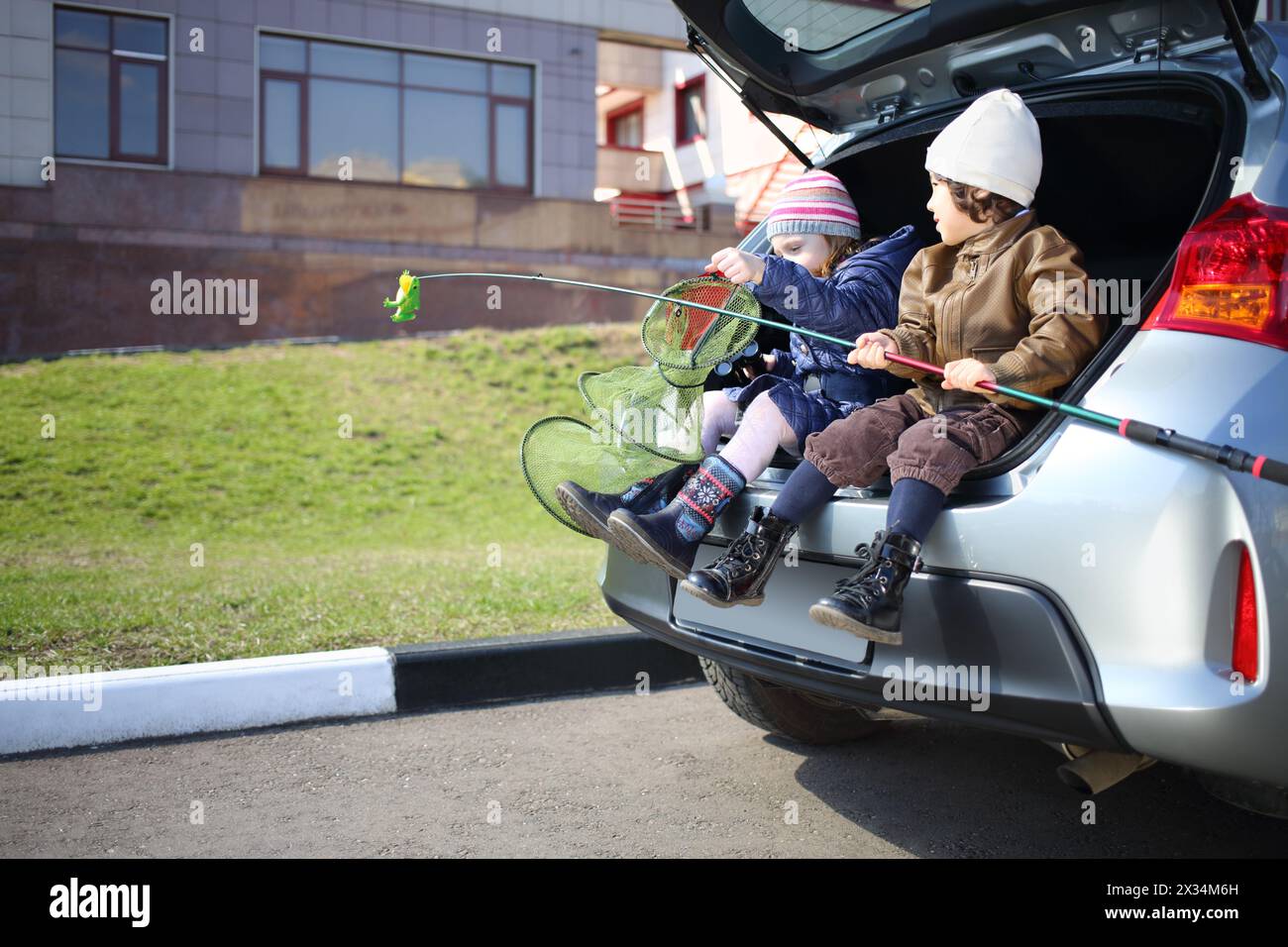 Zwei Kinder sitzen im offenen Kofferraum mit Angelrute und Netz Stockfoto