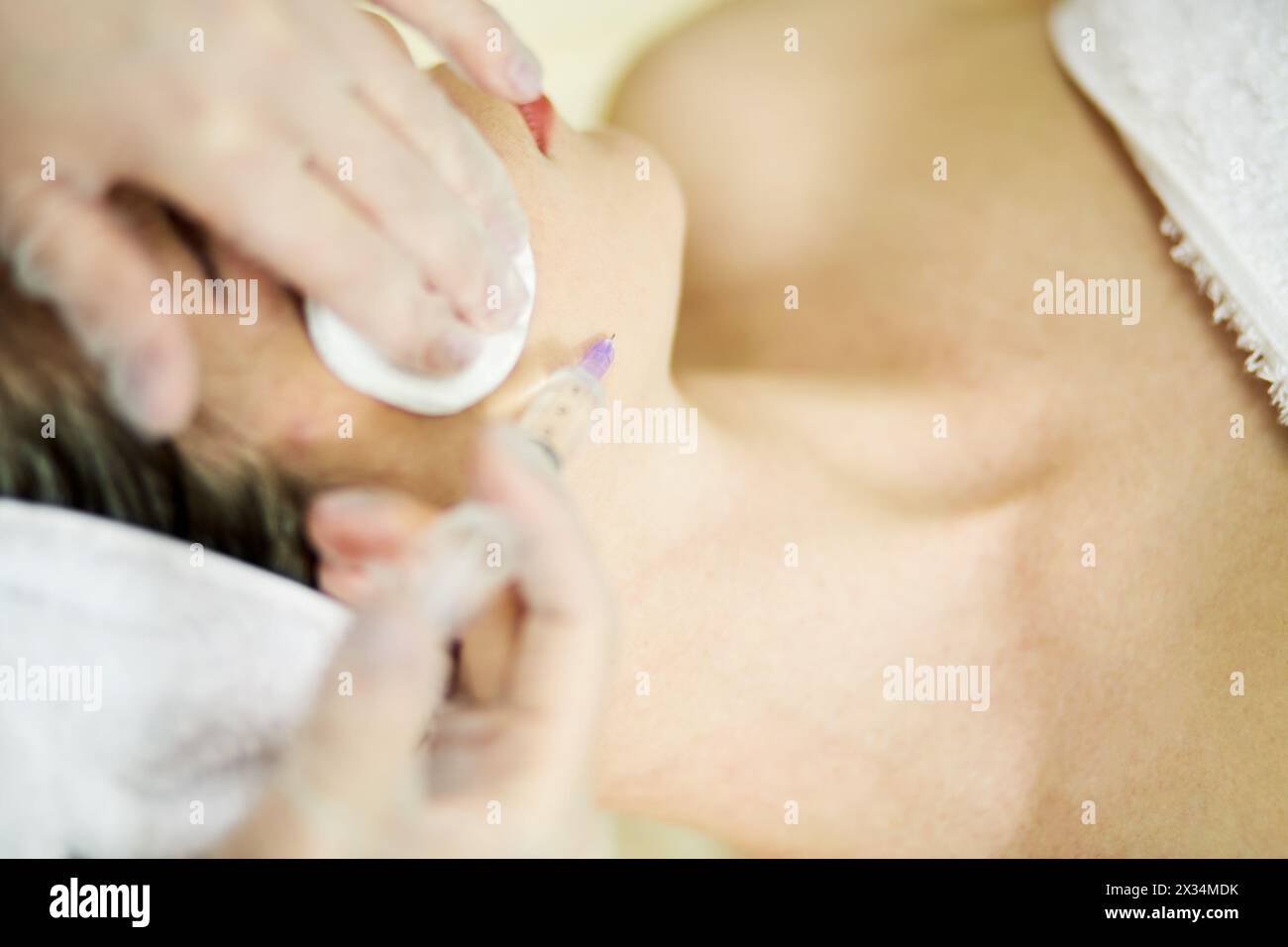 Kosmetikerhände in Gummihandschuhen injizieren Frau, die im Schönheitssalon auf der Couch liegt, unter den Kinnbereich. Stockfoto