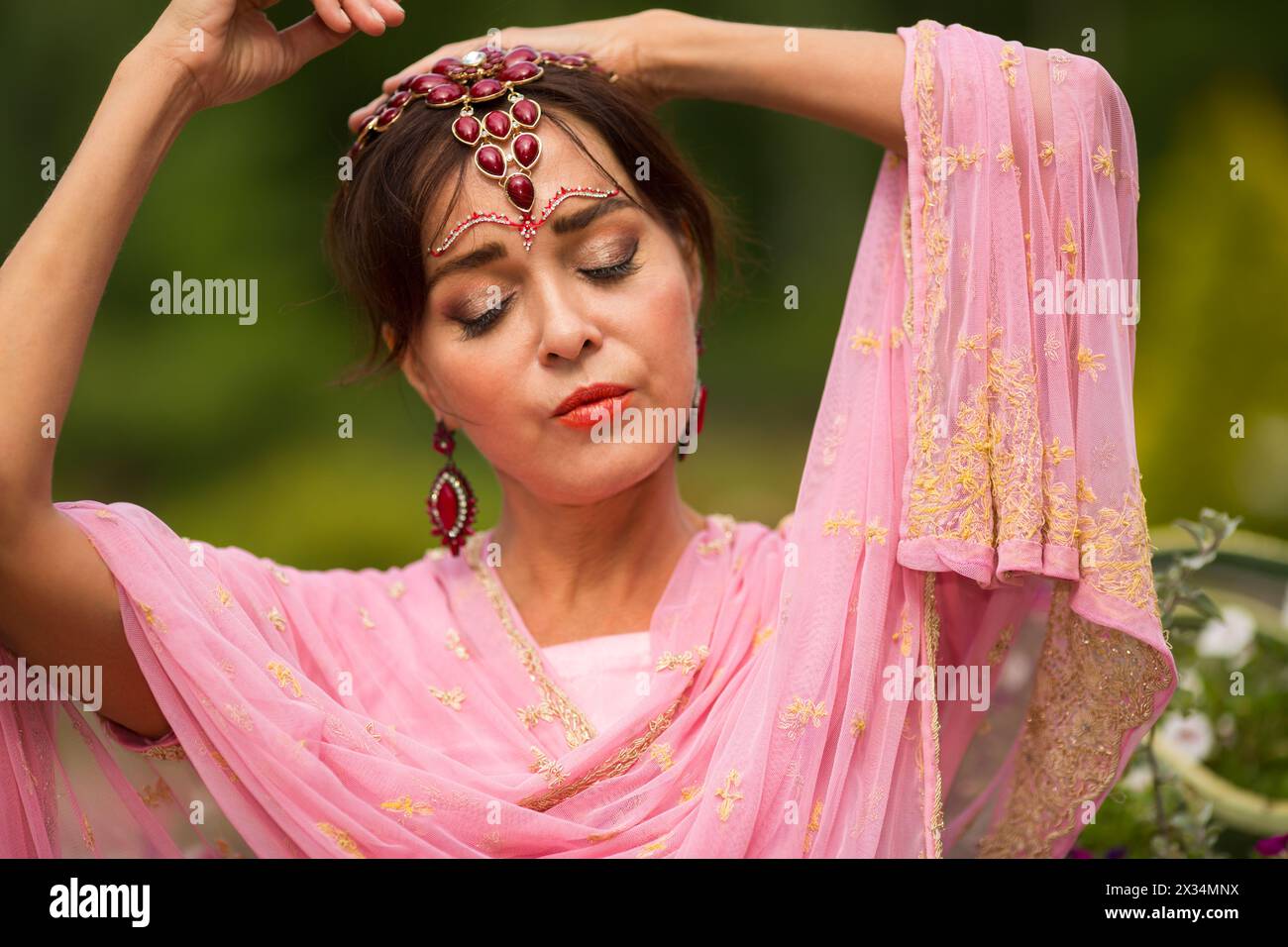 Frau mittleren Alters in rosa Sari und indischer Verzierung posiert im Sommerpark Stockfoto