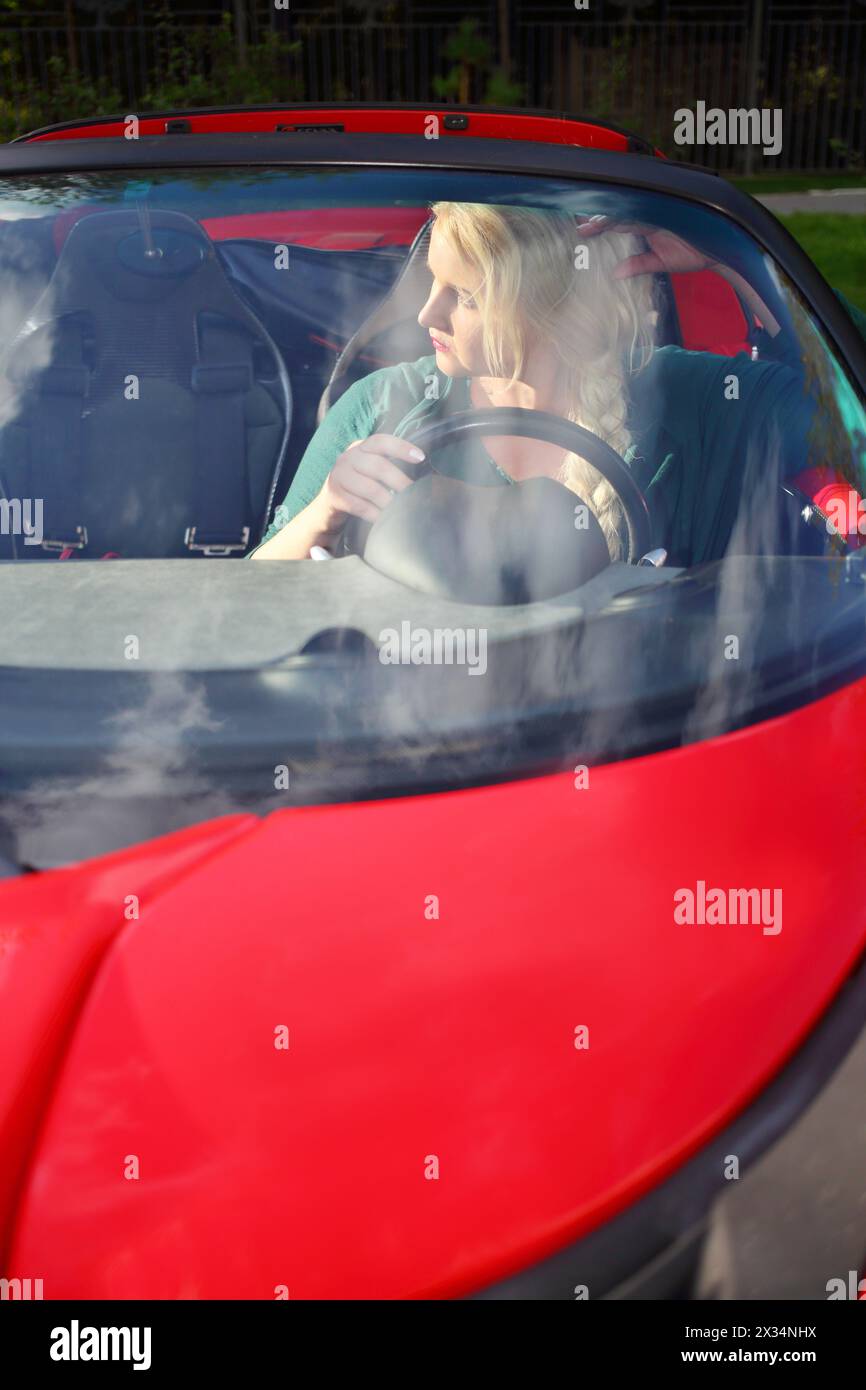 Blonde junge Frau sitzt im roten Sportwagen und schaut am Sommertag weg Stockfoto