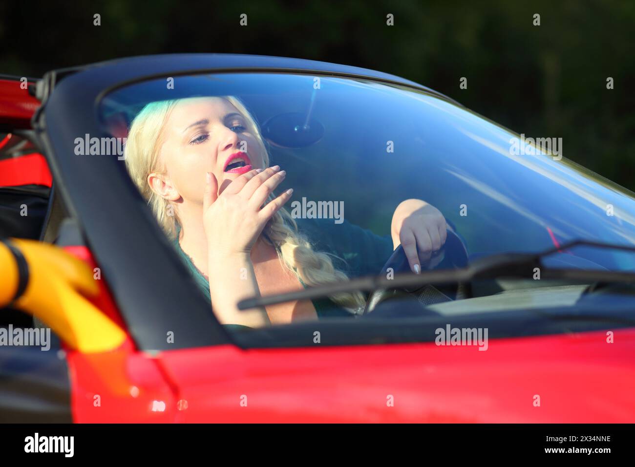 Die blonde hübsche Frau sitzt im roten Sportwagen und schaut an sonnigen Tagen in den Spiegel Stockfoto