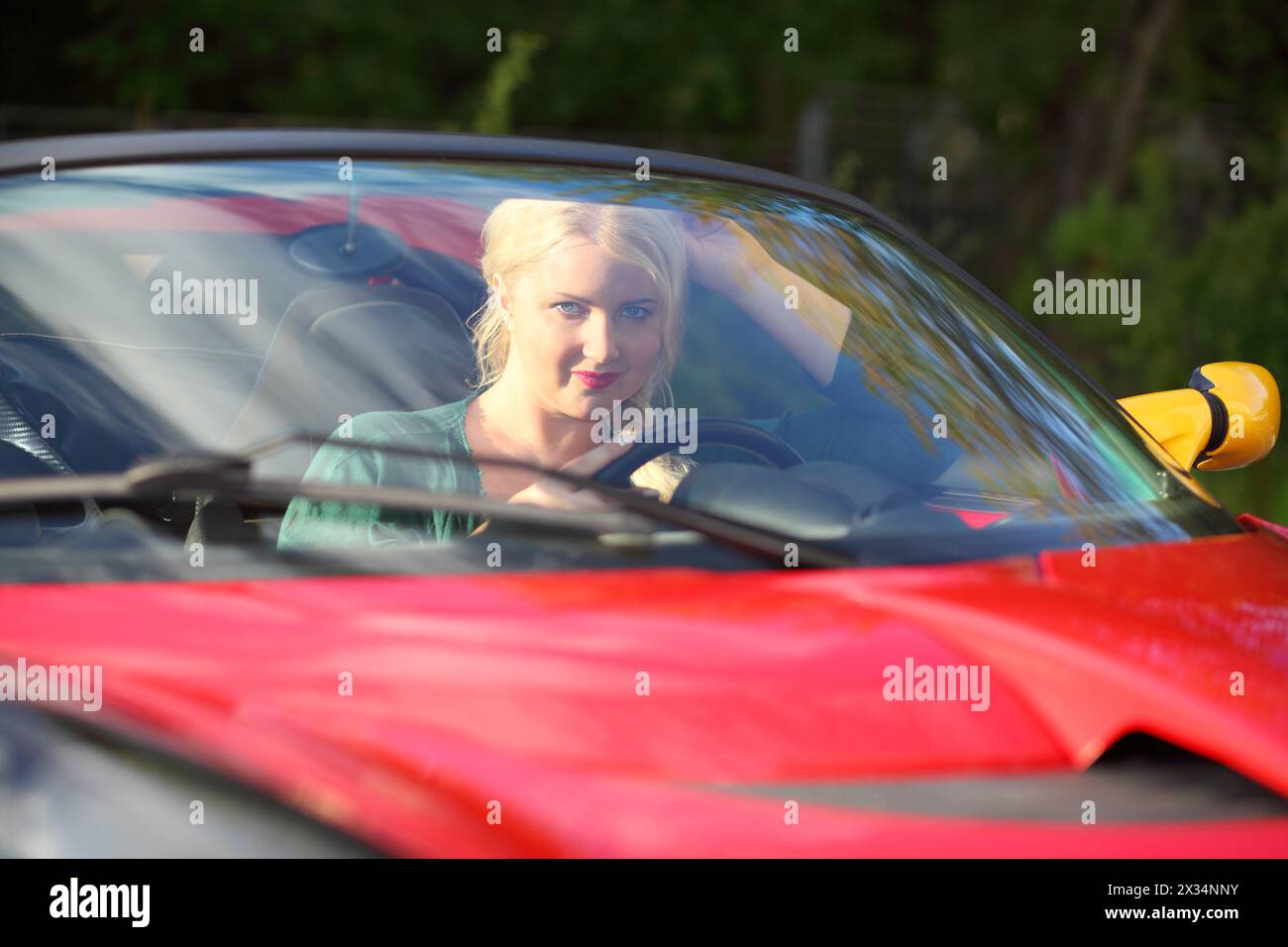 Die blonde hübsche Frau sitzt im roten Sportwagen und schaut an sonnigen Tagen in die Kamera Stockfoto