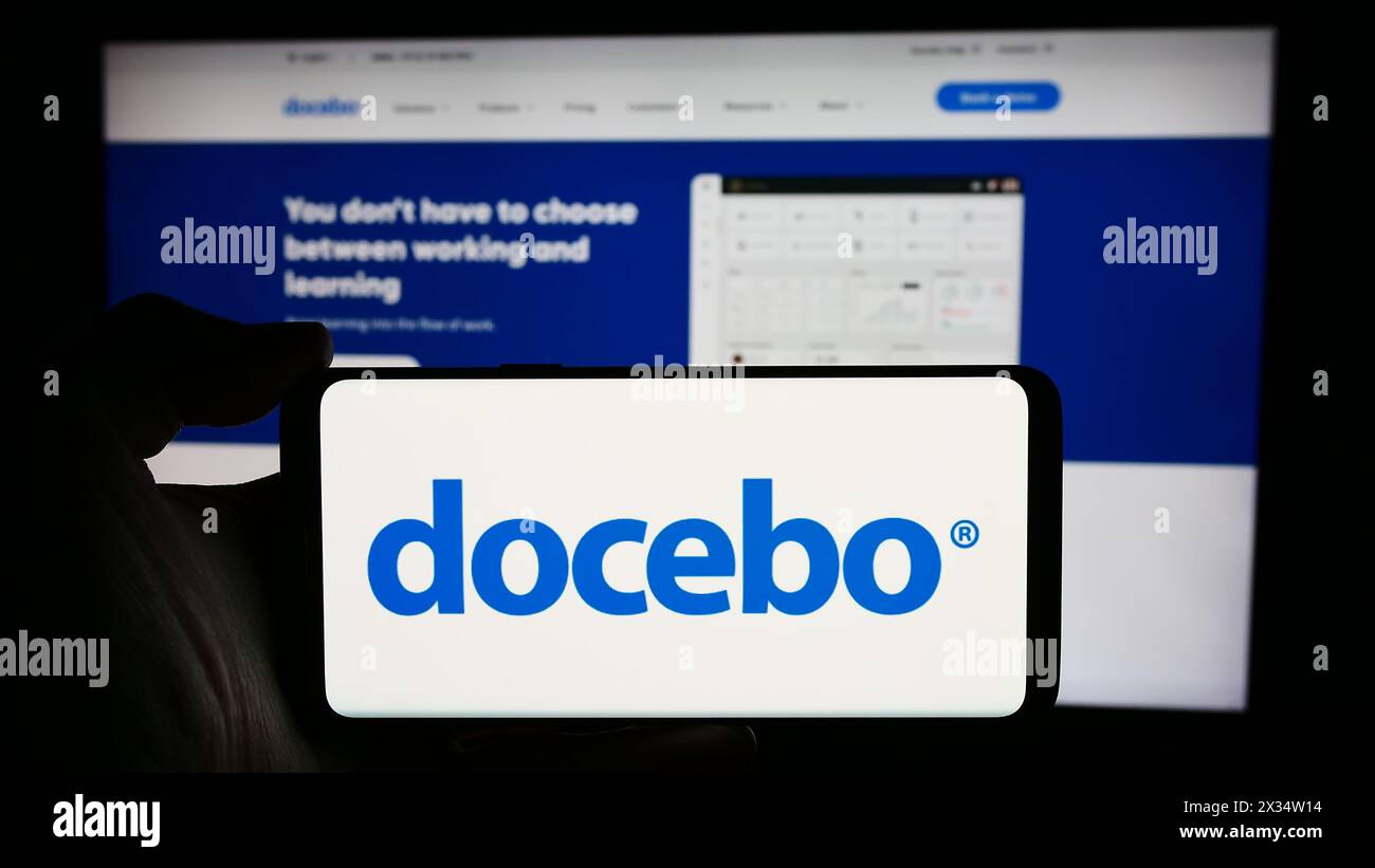 Person, die ein Mobiltelefon mit dem Logo des kanadischen Lernsoftware-Unternehmens Docebo Inc. Vor der Unternehmenswebseite hält. Schwerpunkt auf dem Display des Telefons. Stockfoto