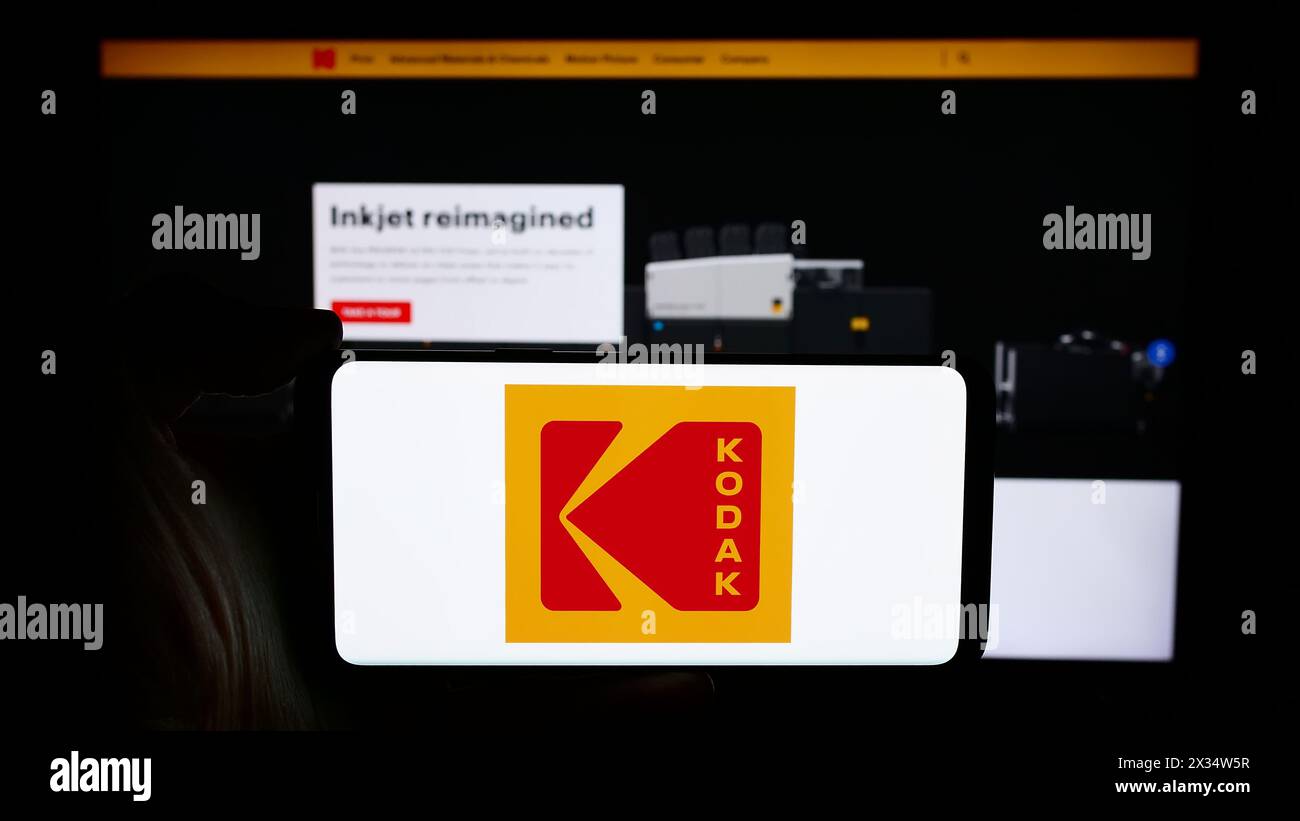 Person, die ein Mobiltelefon mit dem Logo des US-amerikanischen Elektronikunternehmens Eastman Kodak Company vor der Webseite hält. Schwerpunkt auf dem Display des Telefons. Stockfoto