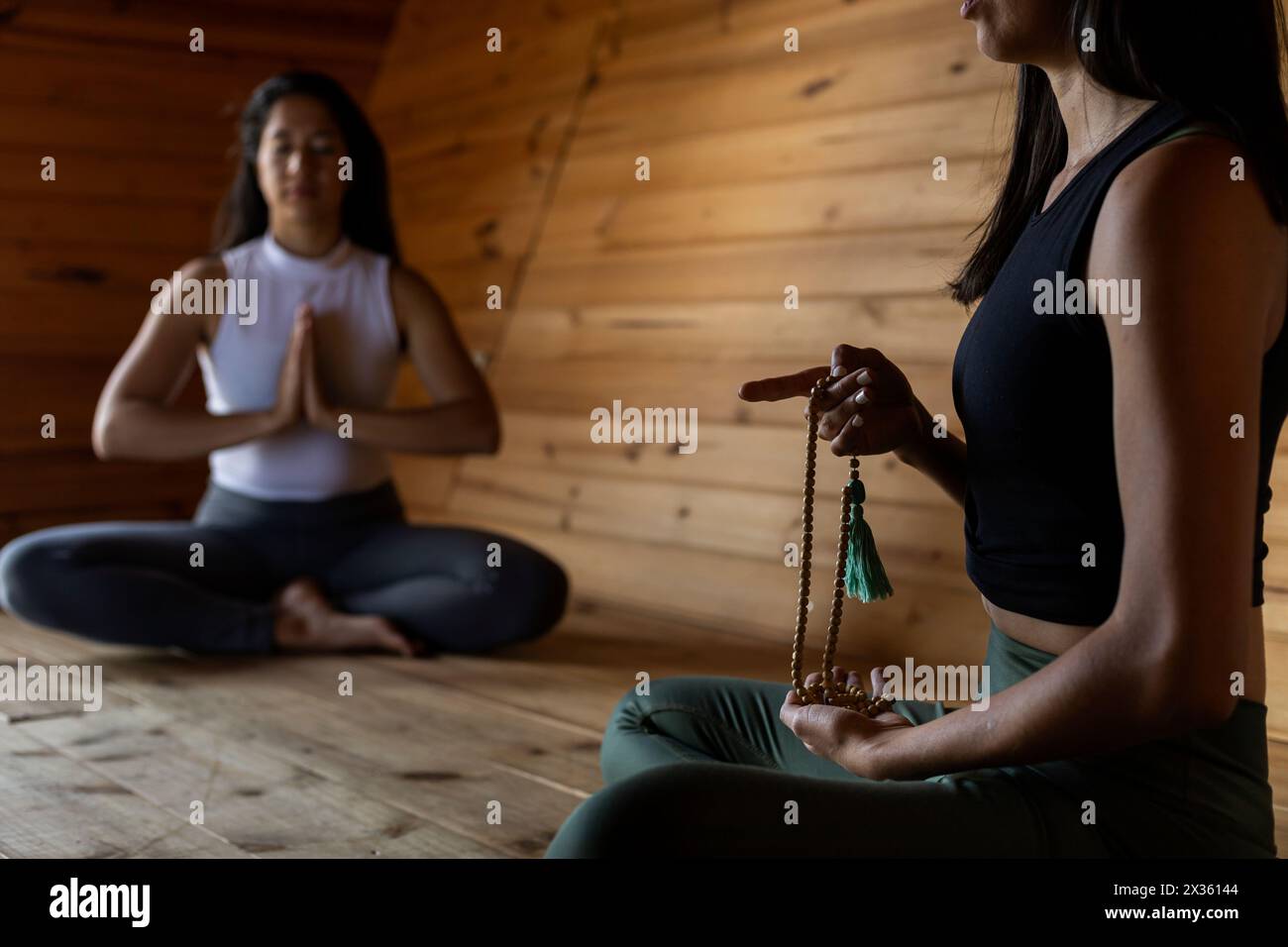 Zwei junge lateinamerikanische Mädchen in Meditationsposition mit einer Japa Mala, einem Meditationsinstrument des Buddhismus. Hintergrund der Holzlatten. Mittel Stockfoto