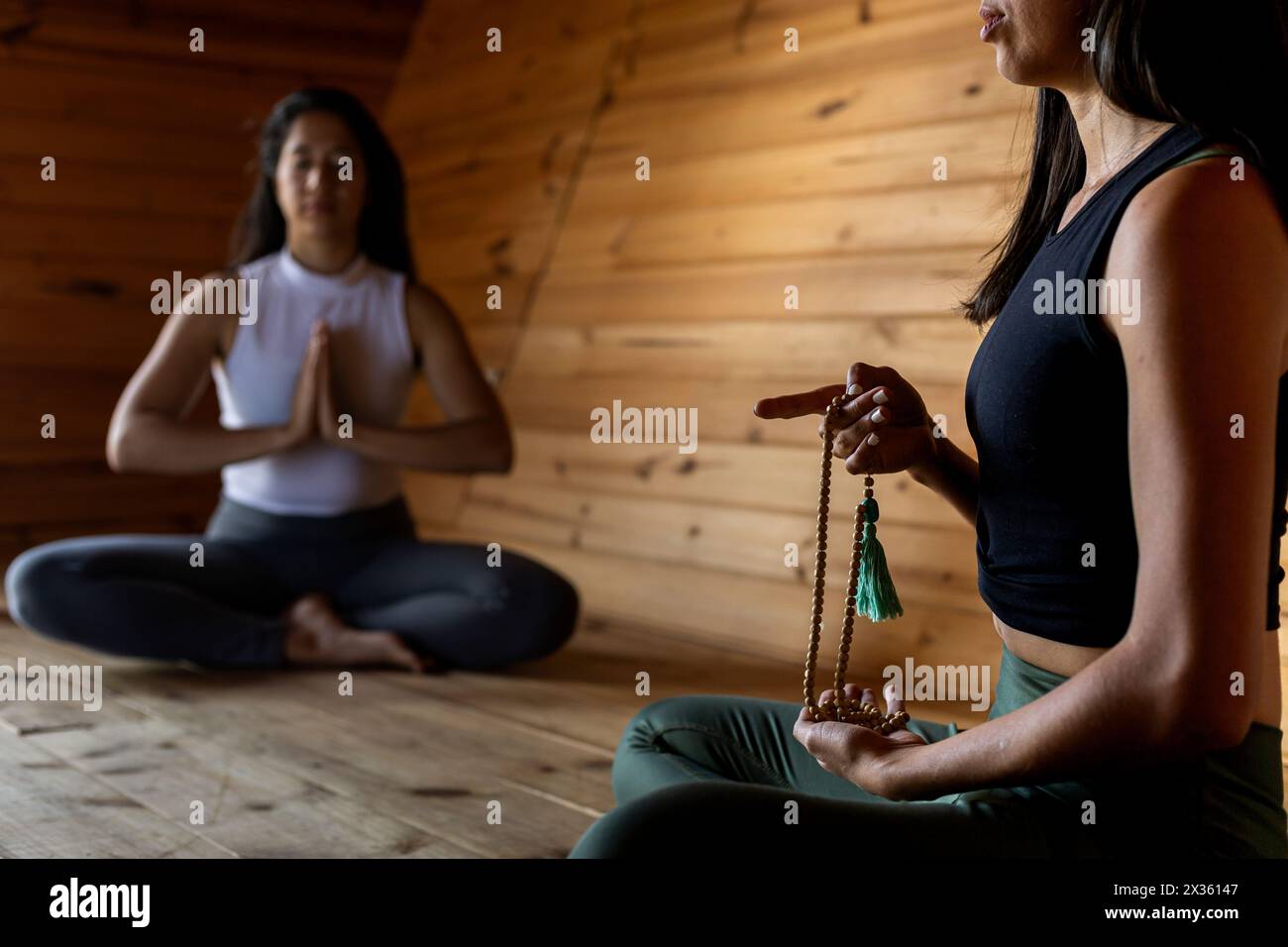 Zwei junge lateinamerikanische Mädchen in Meditationsposition mit einer Japa Mala, einem Meditationsinstrument des Buddhismus. Hintergrund der Holzlatten. Mittel Stockfoto