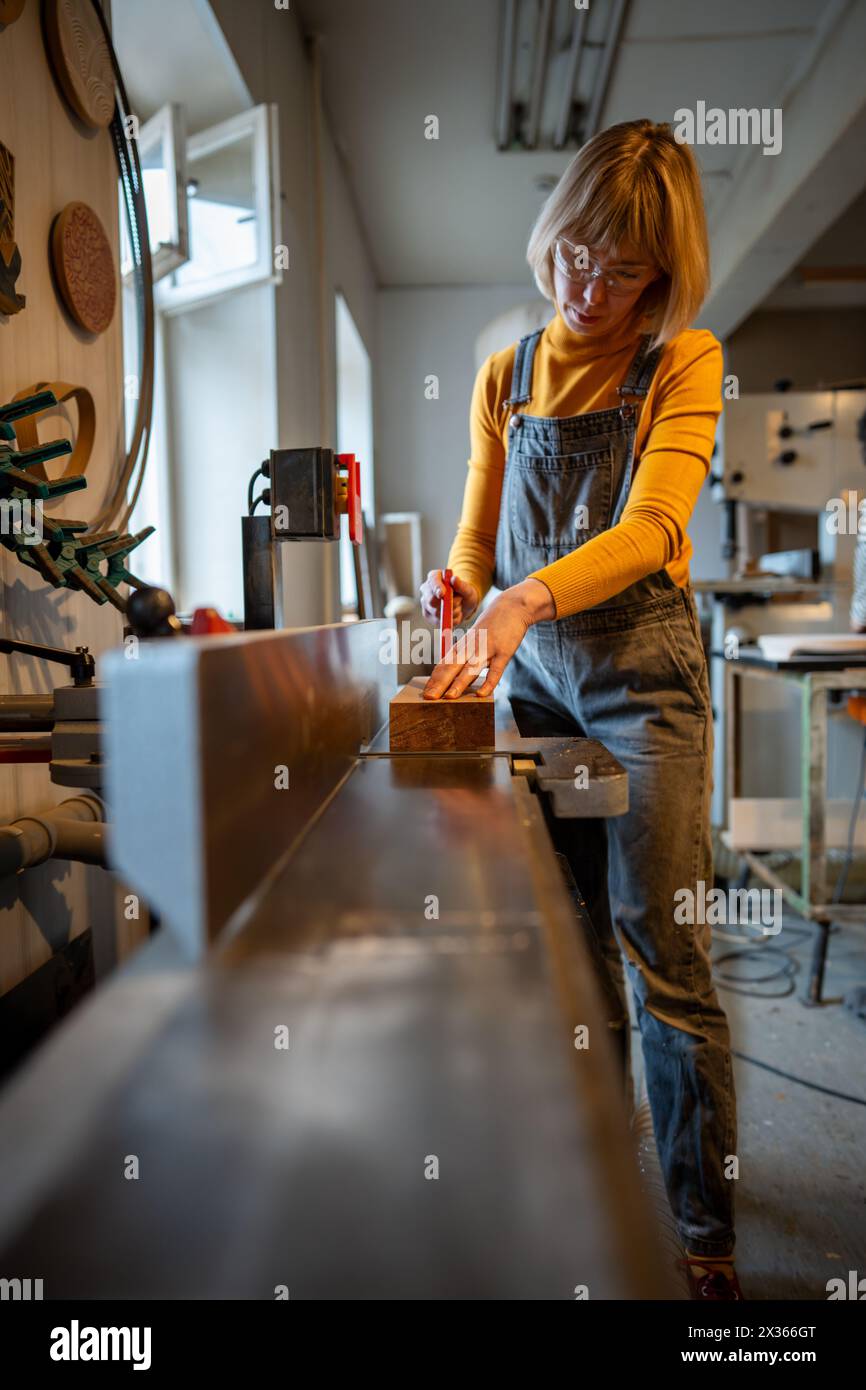 Fokussierte Zimmerfrau, die an einem Elektrohobel arbeitet und eine Schutzbrille mit Spezialausrüstung trägt. Stockfoto