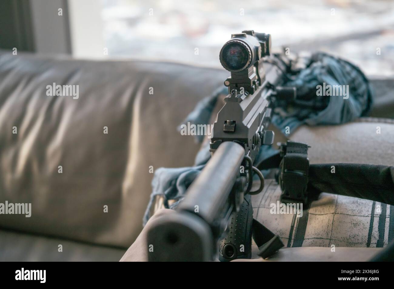 Ein Sturmgewehr mit optischer Sicht auf dem Sofa neben dem Fenster, geringe Schärfentiefe Stockfoto