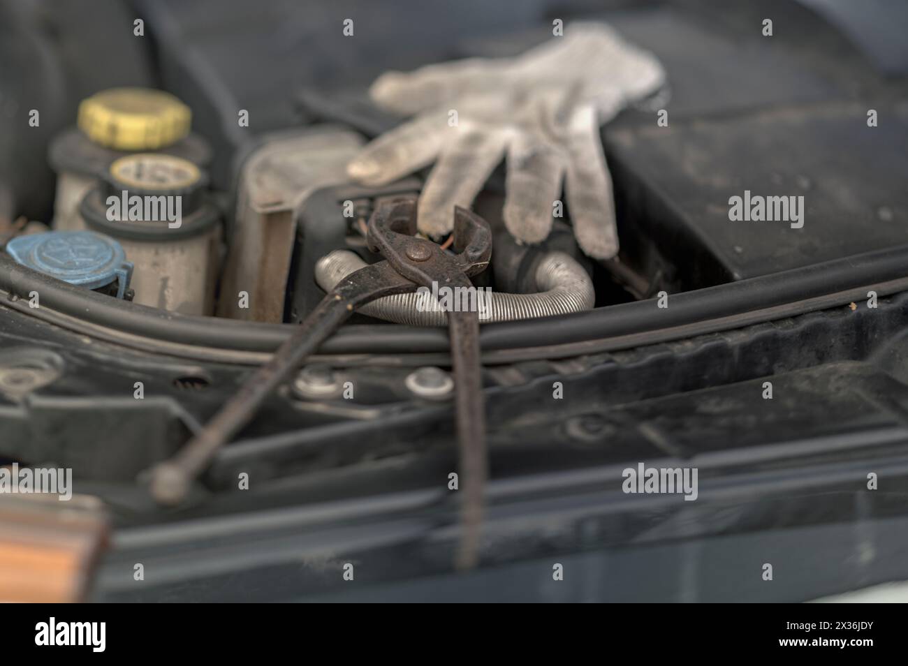 Öffnen Sie die Motorhaube mit einer Zange und Arbeitshandschuhen, die am Motor verbleiben, Außennaht Stockfoto