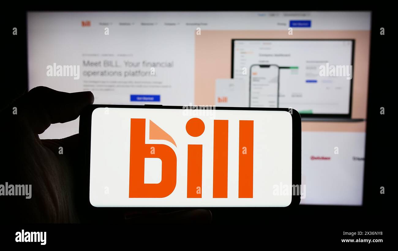 Person, die ein Mobiltelefon mit dem Logo des US-amerikanischen Finanzsoftwareunternehmens BILL Holdings Inc. Vor der Webseite des Unternehmens hält. Schwerpunkt auf dem Display des Telefons. Stockfoto