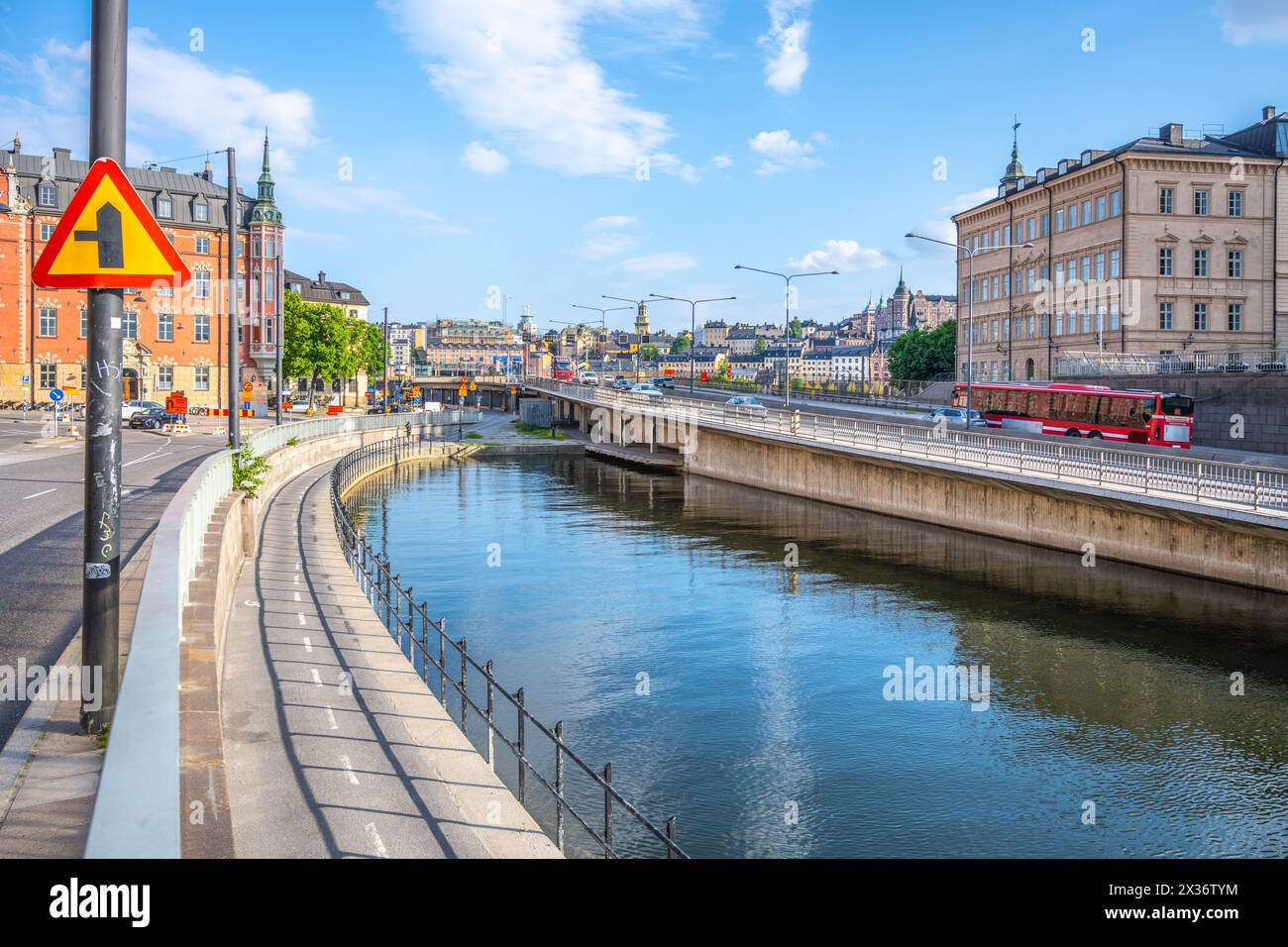 Ein ruhiger Blick auf den Riddarholm Canal mit dem klaren Sommerhimmel, der sich im Wasser spiegelt, umgeben von historischen Gebäuden und einem geschwungenen Fußweg. Stockholm, Schweden Stockfoto