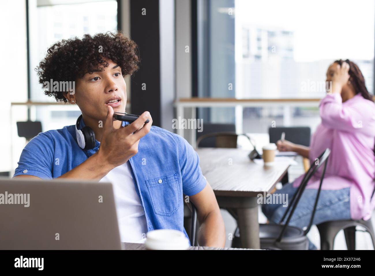 Birassischer Mann mit Kopfhörern spricht auf einem Smartphone, Frau in der Nähe in einem modernen Büro Stockfoto