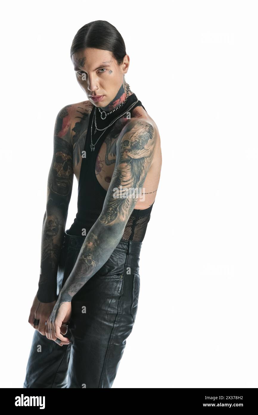 Ein junger Mann mit einem auffälligen Tattoo am Arm steht selbstbewusst in einem Studio-Setting. Stockfoto