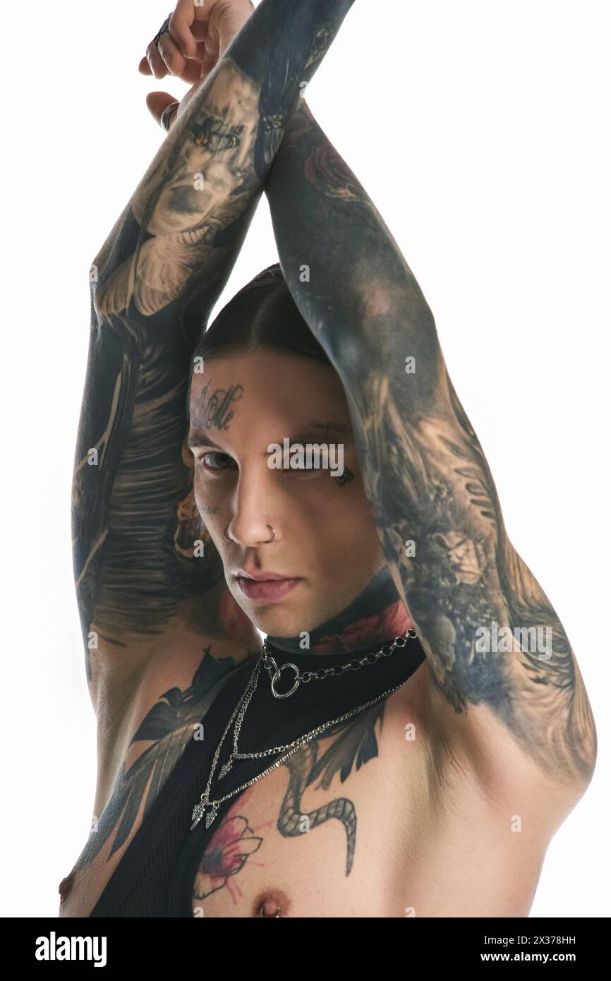 Ein junger, stilvoller Mann mit umfangreichen Tätowierungen und Piercings auf den Armen posiert in einem Studio vor grauem Hintergrund. Stockfoto