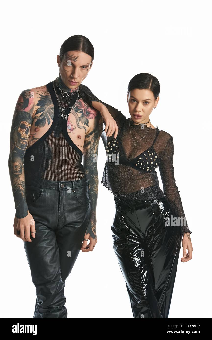 Ein junger, stilvoller Mann und eine Frau mit Tattoos stehen in einem Studio vor grauem Hintergrund zusammen. Stockfoto