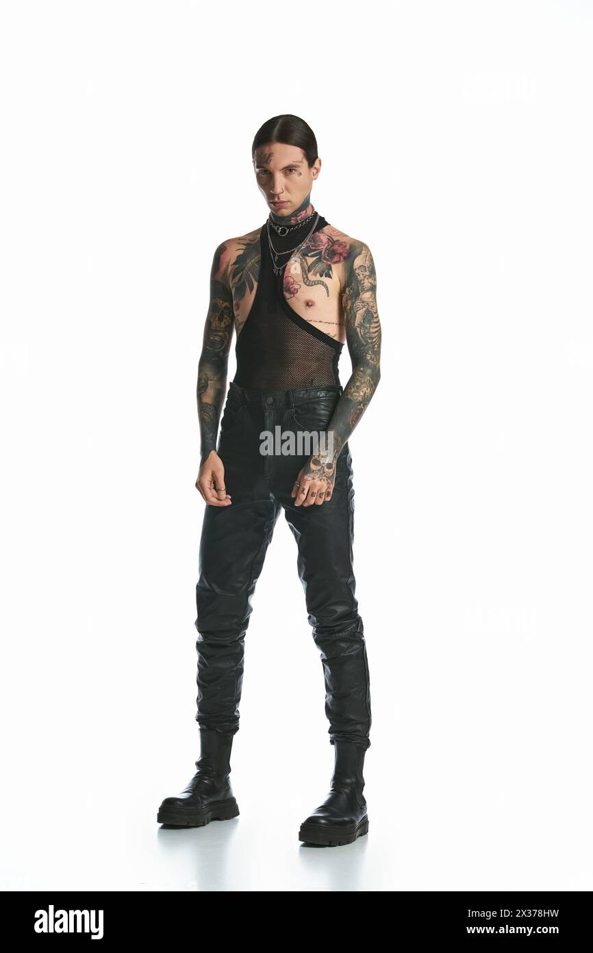 Ein junger Mann mit Tätowierungen posiert selbstbewusst vor einem weißen Hintergrund. Stockfoto