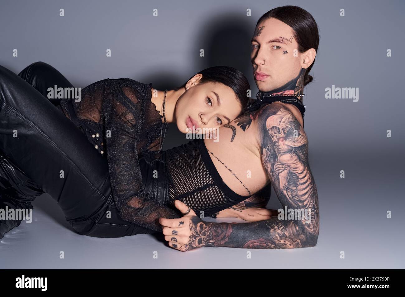 Ein junges tätowiertes Paar posiert in einem Studio vor grauem Hintergrund. Stockfoto