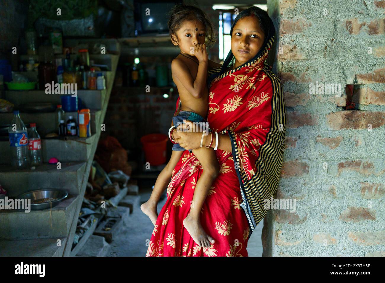 Sundarbans, Indien - 23. Oktober 2023: Nahaufnahme eines Porträts einer jungen indianerin, die ihre Tochter in einem traditionellen Sari hält und in die Kamera blickt Stockfoto