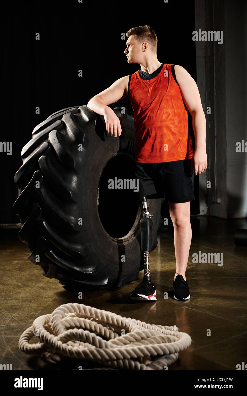 Ein Mann, der stolz neben einem kolossalen Reifen steht und Stärke und Entschlossenheit in einem Moment des Triumphes zeigt. Stockfoto
