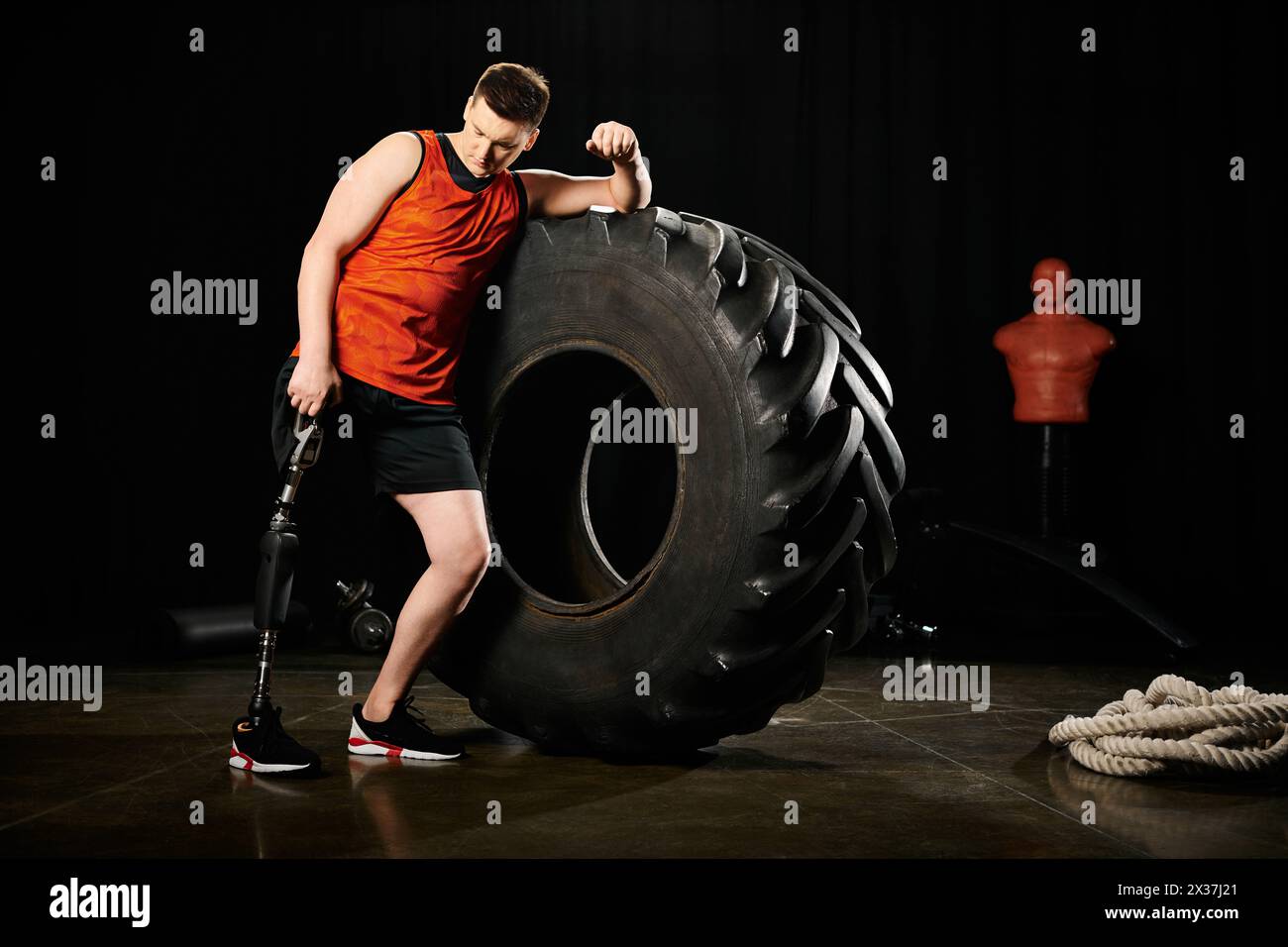 Ein Mann mit einer Beinprothese steht stolz neben einem riesigen Reifen und zeigt Stärke und Ausdauer. Stockfoto