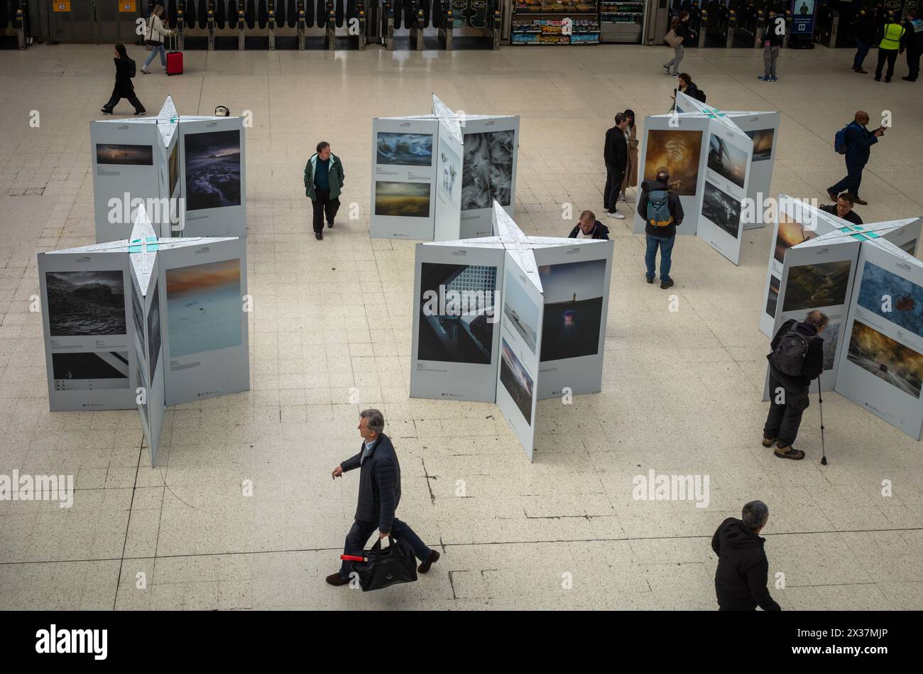 Passagiere gehen an einer Fotoausstellung in der Halle der Waterloo Station, London, UK, vorbei Stockfoto