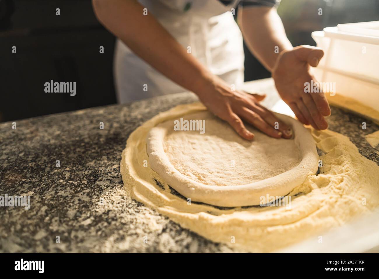 Zubereitung von Pizzateig – Nahaufnahmen der Hände beim Kneten und Dehnen von Pizzateig auf einer bemehlten Oberfläche, die die Haptik und das Anfassen des Prozesses betonen. Hochwertige Fotos Stockfoto