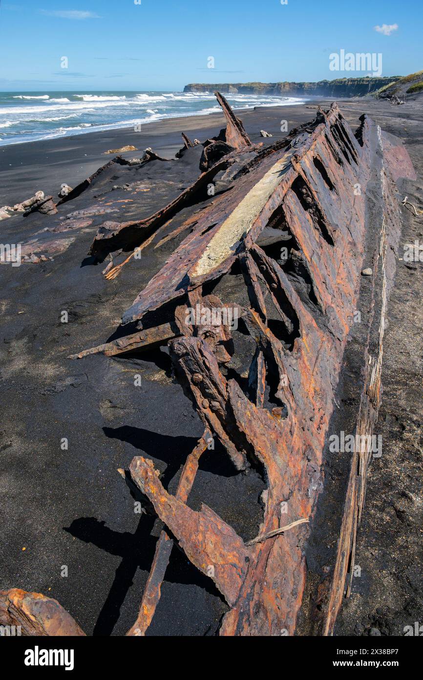 Der rostende Rumpf eines Bootes, das halb im schwarzen Sand von Patea Beach, Taranaki, Nordinsel, Neuseeland begraben ist Stockfoto