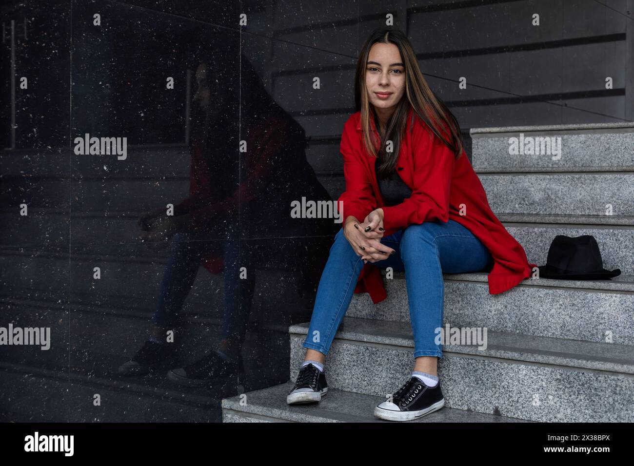 Porträt einer jungen lateinamerikanischen Frau, die auf der Treppe sitzt. Posiert mit positiver und selbstbewusster Einstellung. Porträt-Konzept Stockfoto