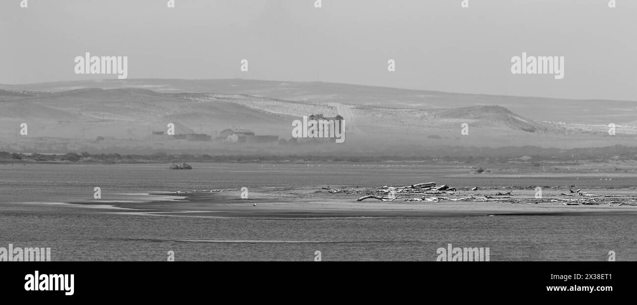 Die Nebellichtung zeigt eine freiliegende Sandbank mit Treibholz und die verlassenen Gebäude und Halden aus den alten Diamantenminen, über der Orange Stockfoto