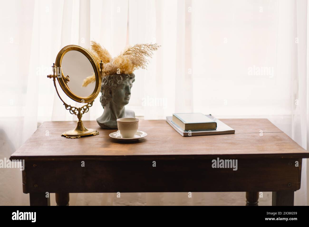 Eleganter Vintage-Spiegel und Büstenvase mit Pampas-Gras neben einer Kaffeetasse auf einem Holztisch Stockfoto