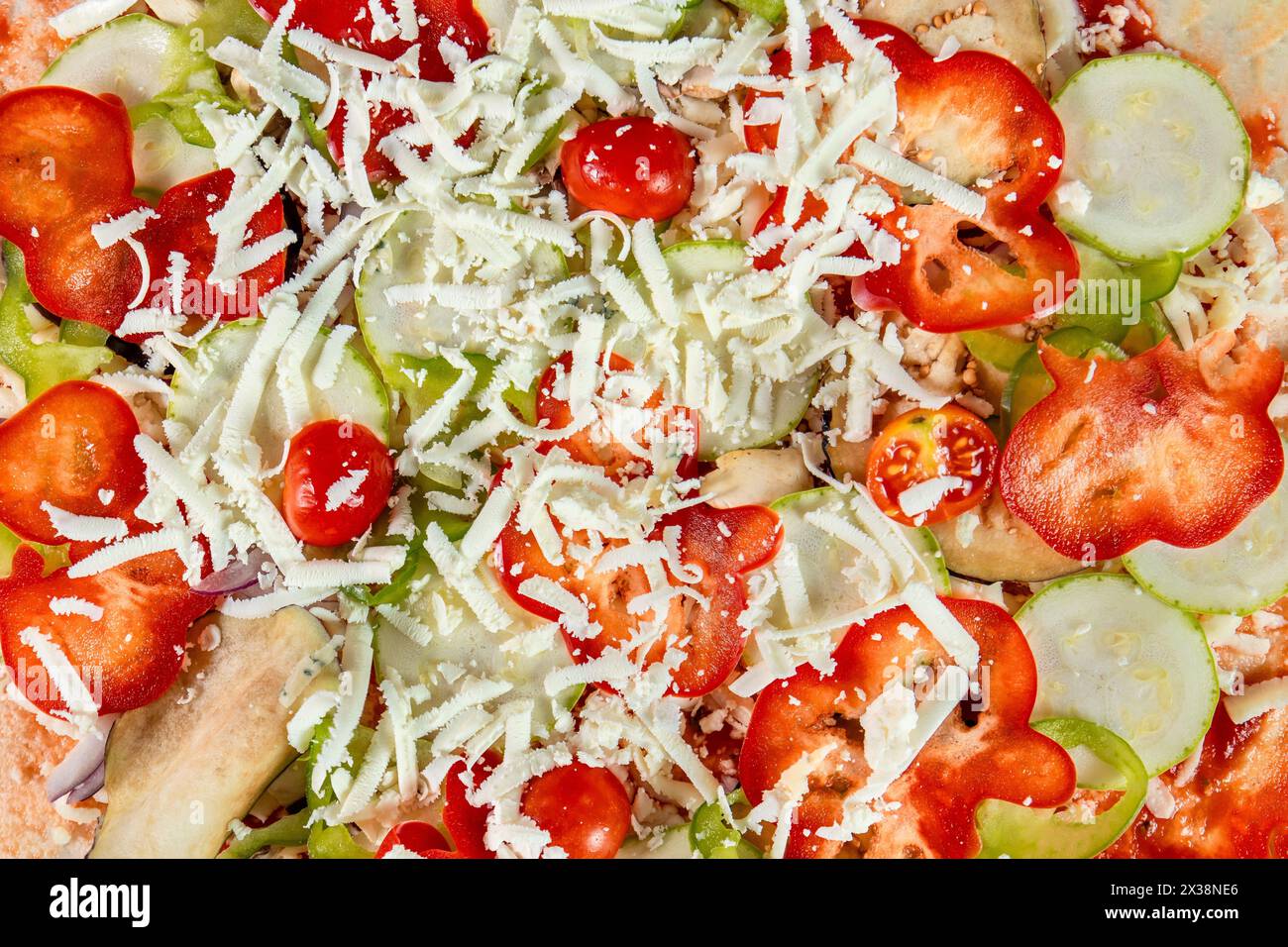 Ein Nahaufnahme einer vegetarischen Pizza vor dem Backen, mit Mozzarella, Tomaten, roten und grünen Paprika und Gurkenscheiben, arran Stockfoto