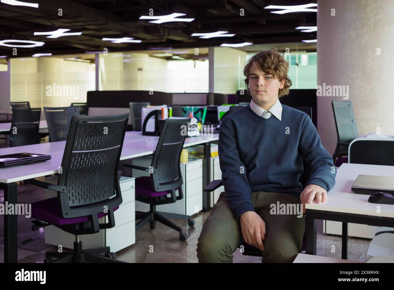 Hübscher Teenager sitzt in einem modernen Büro mit vielen Arbeitsplätzen Stockfoto