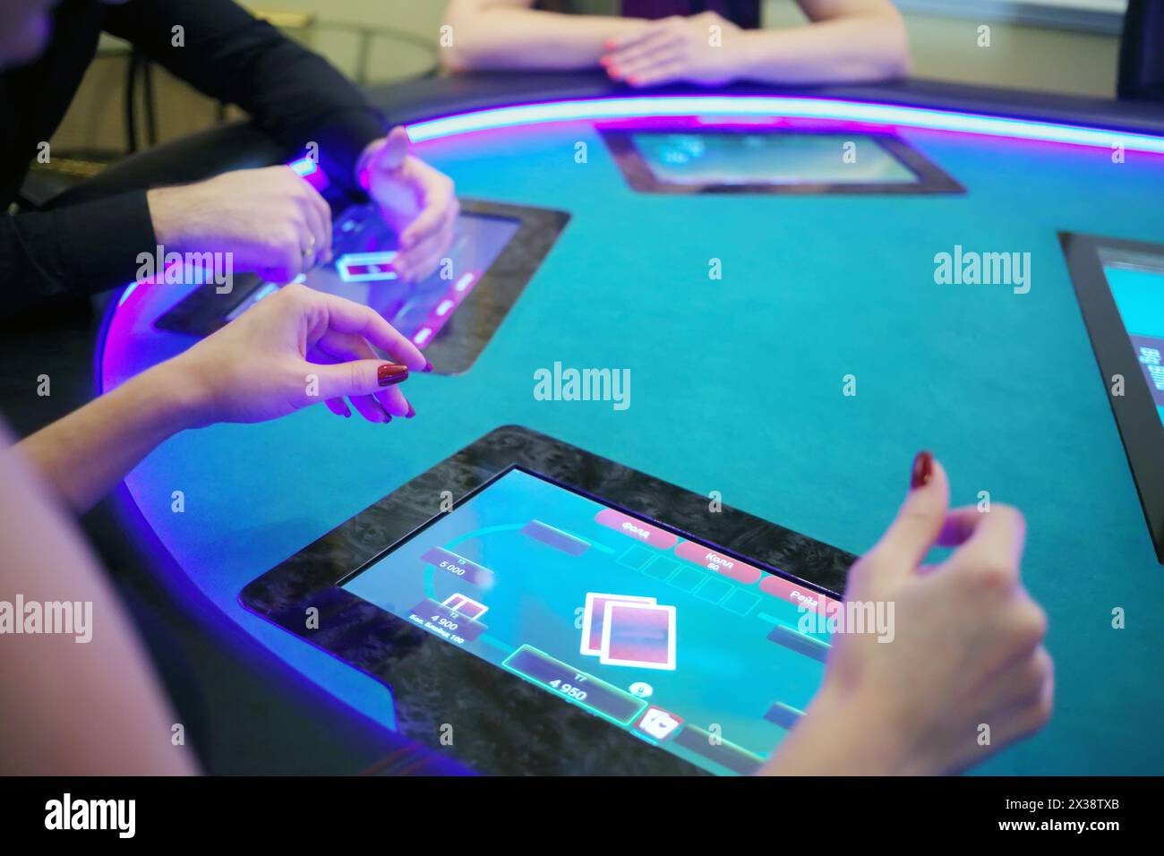 Hände von zwei Frauen und Männern spielen Poker im Casino mit elektronischem Tisch, Fokus auf Frauenhand Stockfoto