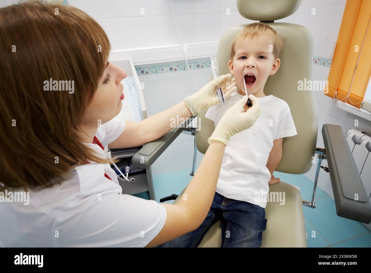 Arzt untersucht den Mund des Kindes, das im medizinischen Sessel sitzt. Stockfoto