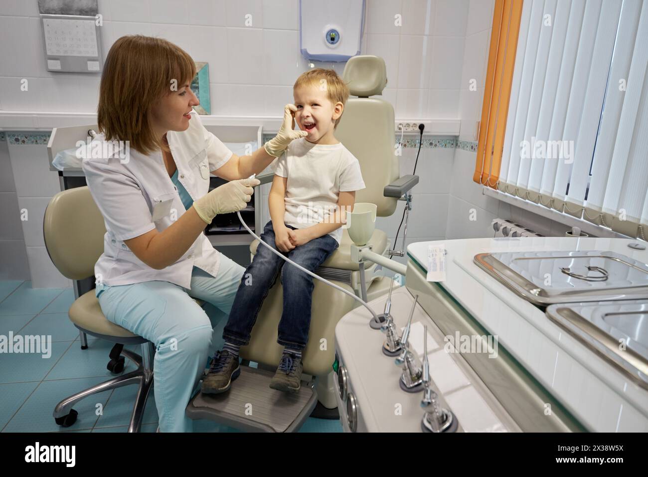 Weibliche Ärztin untersucht den Mund des Jungen, der im medizinischen Sessel sitzt. Stockfoto