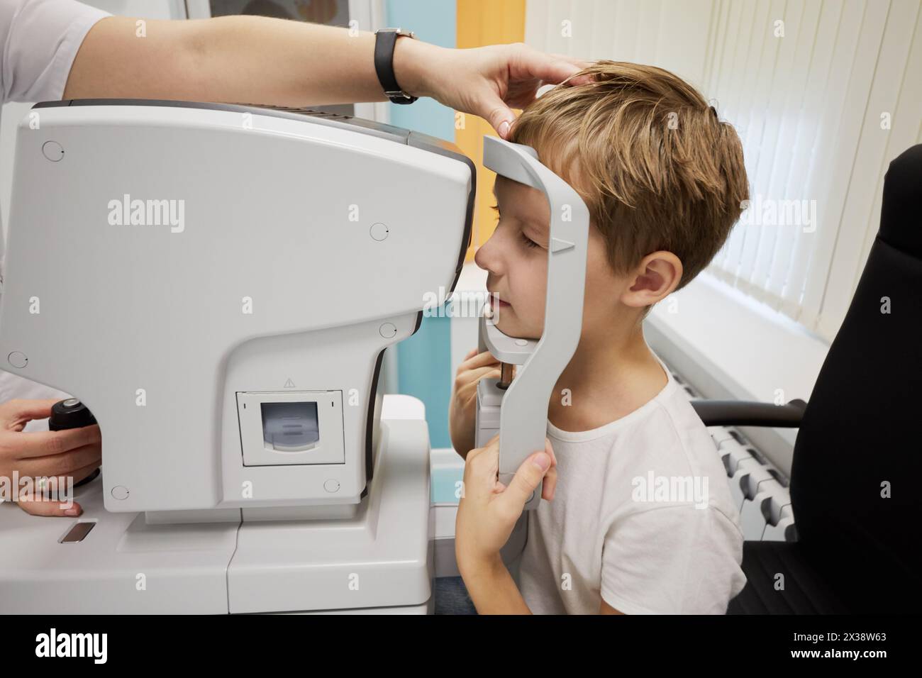 Hände von Ärztin und Jungen beim Blick ins Keratometer-Okular. Stockfoto