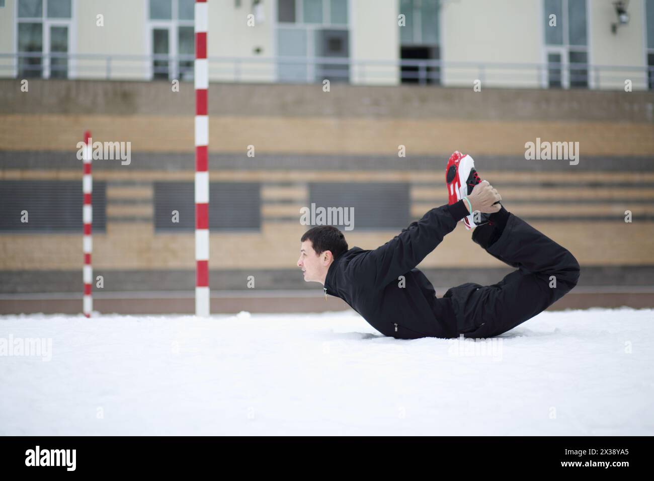 Ein Mann in Schwarz macht Übungen auf dem Spielplatz in der Nähe des Gebäudes am Wintertag Stockfoto