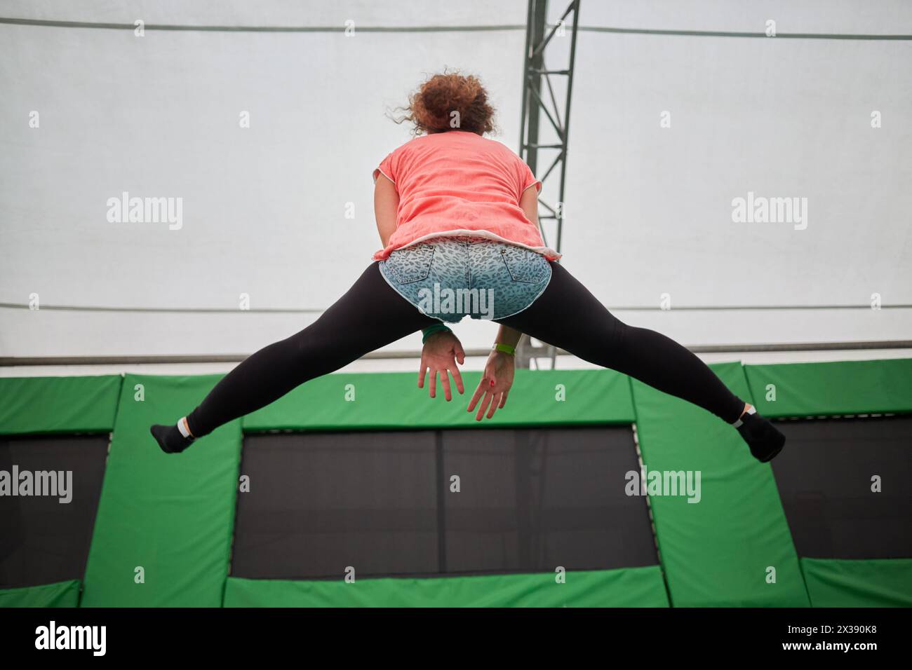 Die junge Frau springt auf Trampolin und macht einen Splitt, Rückansicht. Stockfoto