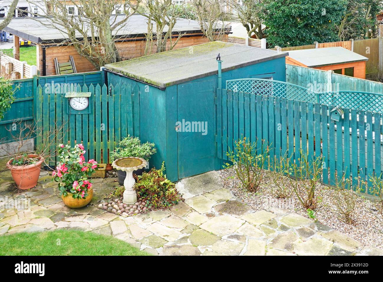 Vier verschiedene Nachbarn treffen auf die Begrenzungslinien des Gartenzauns, die teilweise durch Weißdornhecke getrennt sind, kleine bis sehr große Schuppen im Frühjahr England UK Stockfoto