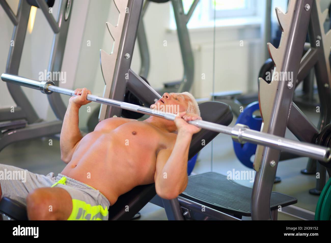 Ein Mann mittleren Alters in Hosen hebt die Bar in einem modernen Fitnessstudio auf, flaches dof Stockfoto